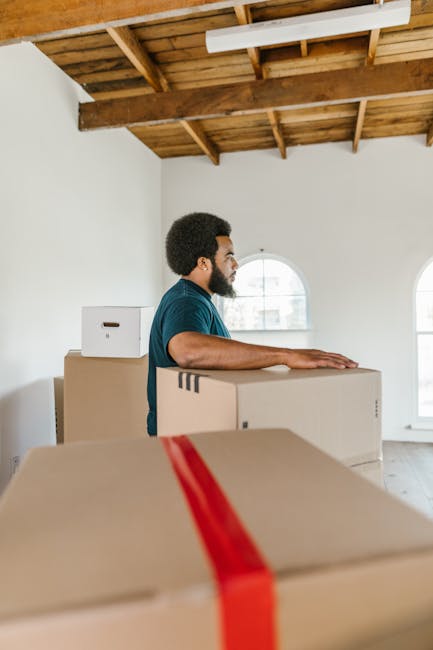 A professional mover from Man with Van Coney Hall, dressed in a navy blue uniform, is inside a property during a home relocation. He is holding a clipboard and appears to be reviewing a checklist abou